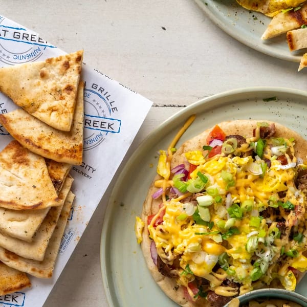 A breakfast pita with scrambled eggs, cheese, bacon, and scallions, next to pita bread.