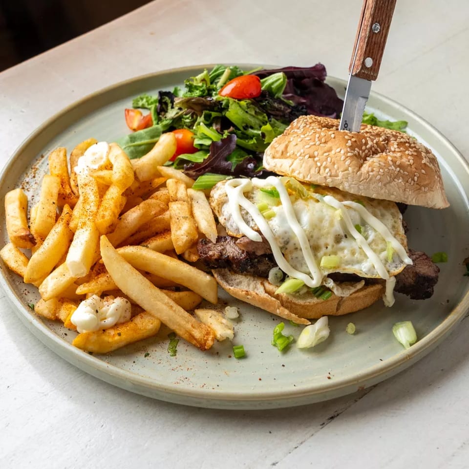 A steak burger with a fried egg, fries, and a side salad on a gray plate.