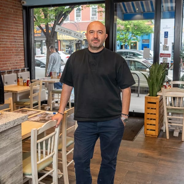 A bald man in a black shirt and blue pants stands in a restaurant dining area.