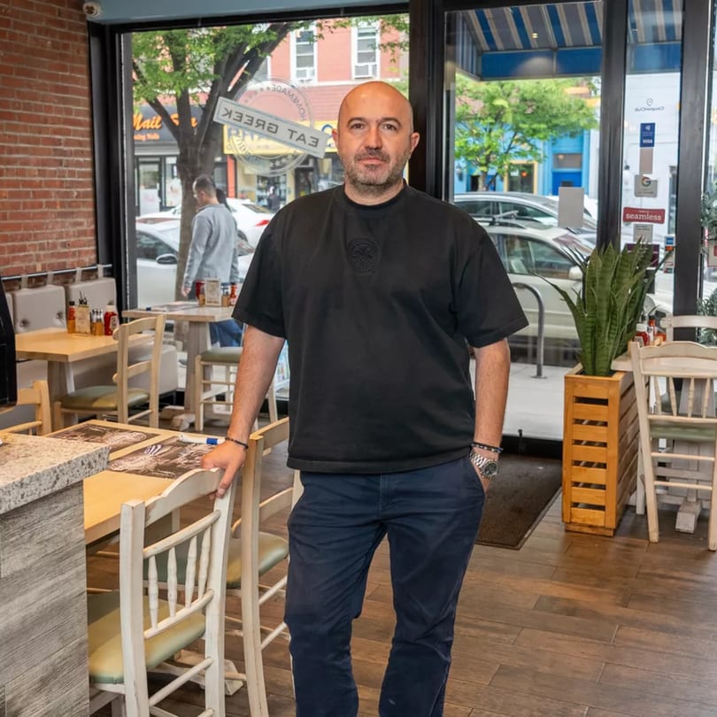 A bald man in a black shirt and blue pants stands in a restaurant dining area.