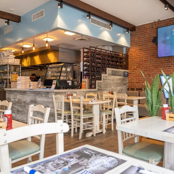 Bright, modern restaurant interior with light blue walls, wooden tables, white chairs, and an open kitchen.